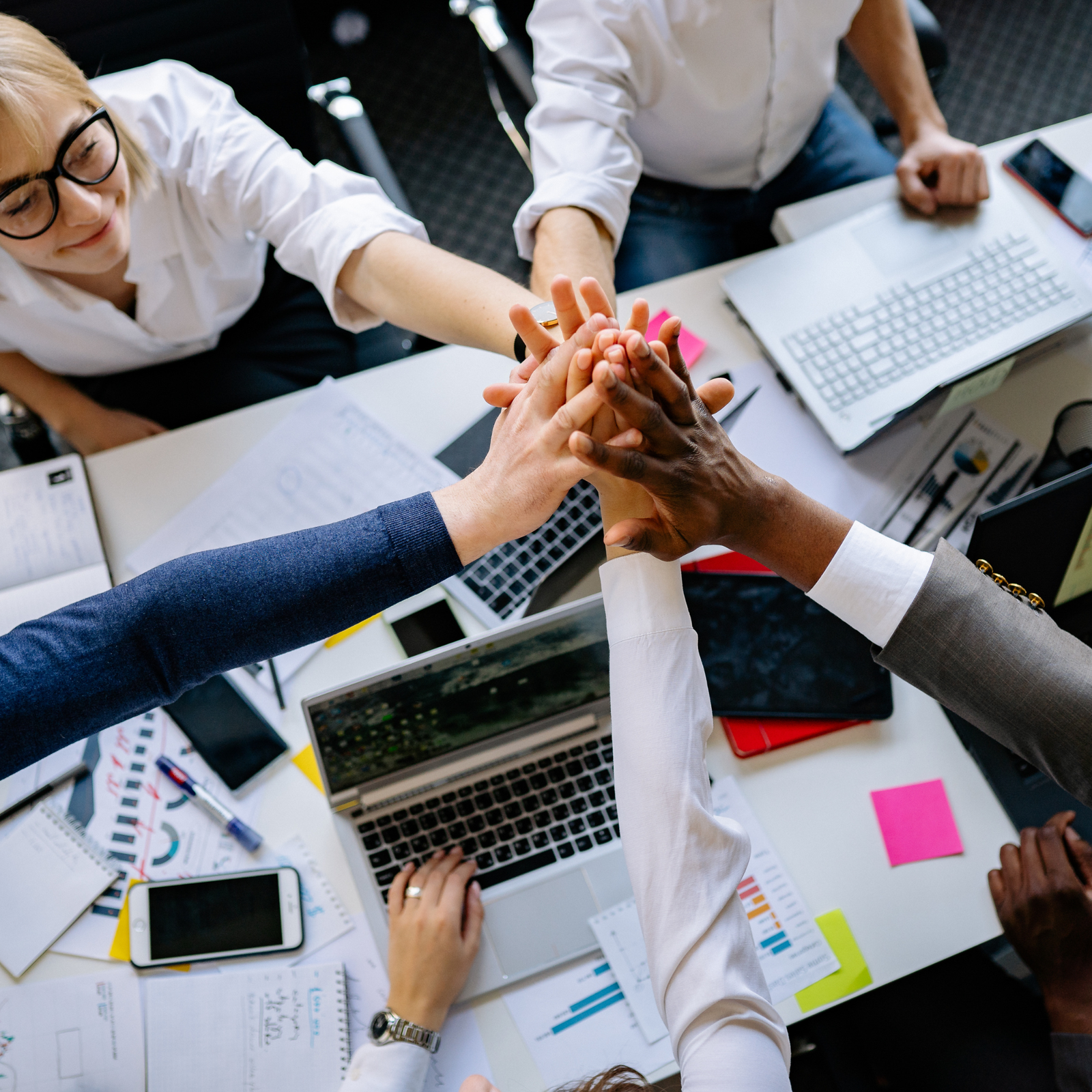 Diverse hands stacked together in a team huddle over a meeting table, symbolizing collaboration and partnership